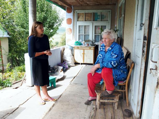 Catea trifft eine ältere Frau vor ihrem Haus und bringt eine warme Mahlzeit